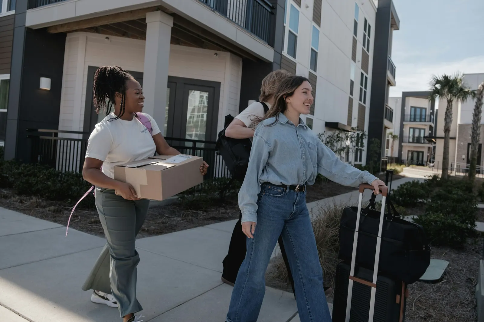Young people carrying boxes and luggage towards an apartment building