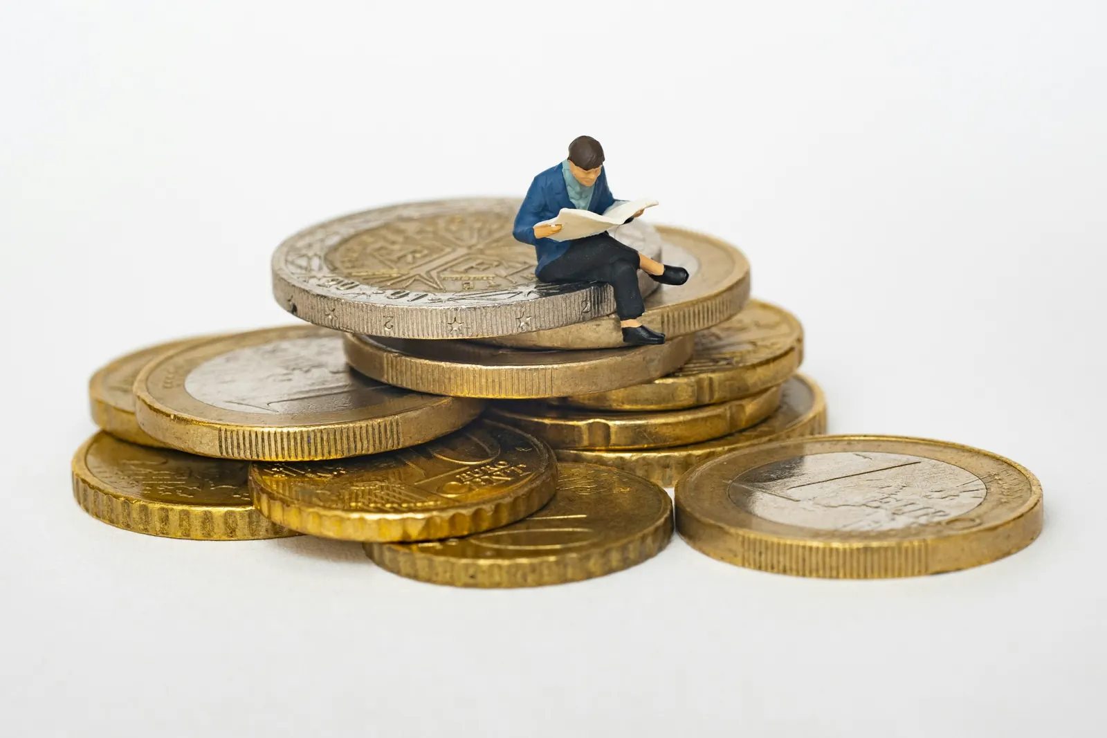 Miniaturfigur sitzt auf einem Stapel Euromünzen und liest Zeitung