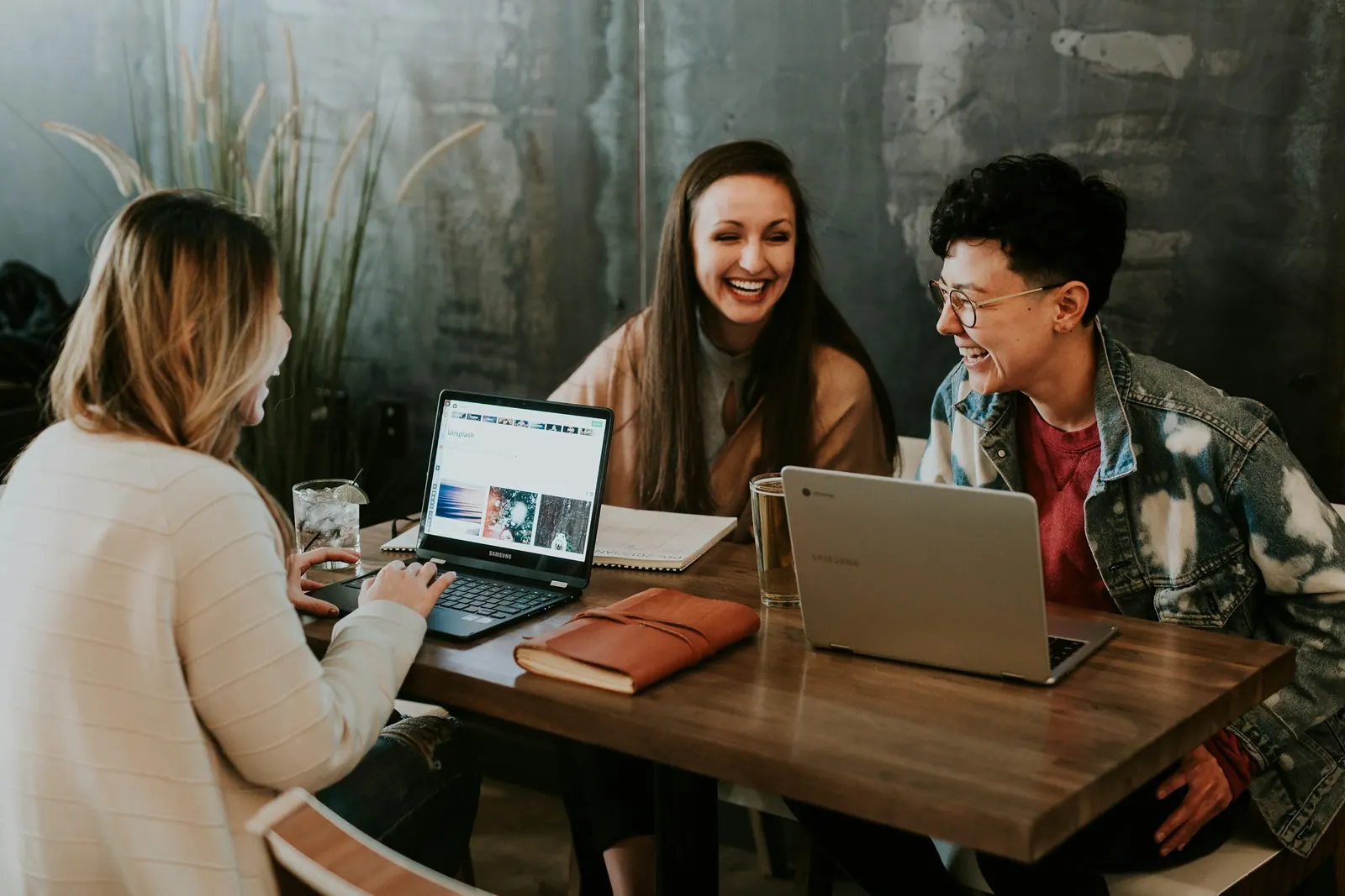Drei junge Menschen lachen an einem Tisch mit Laptops