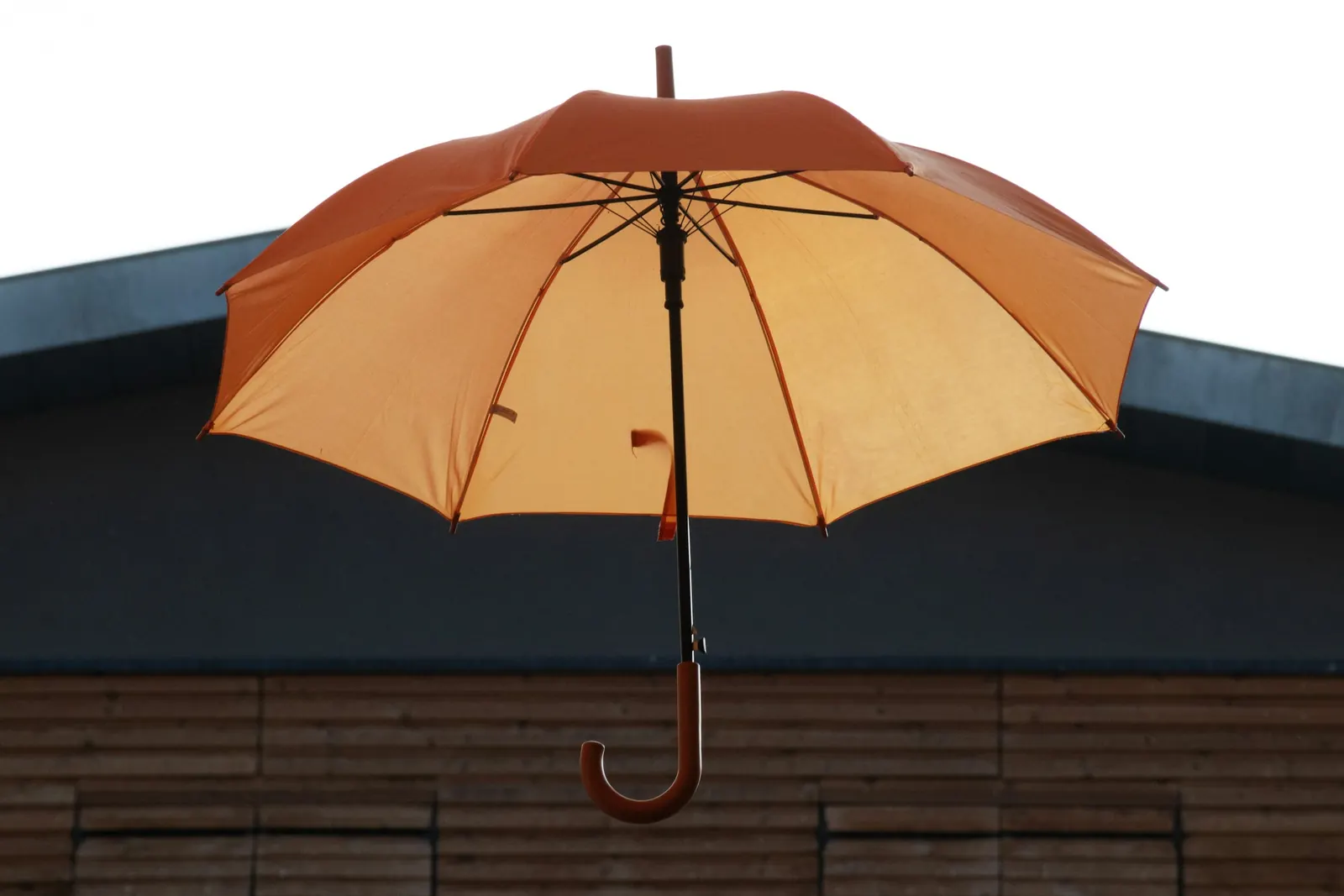 Aufgespannter orangefarbener Regenschirm vor einem Dach